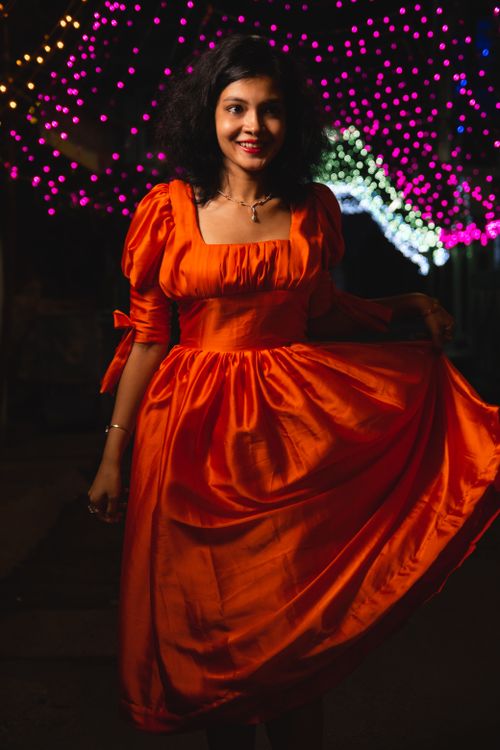 Free Charming woman posing in a striking red dress under colorful evening lights, exuding elegance and joy. Stock Photo