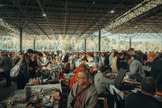 Bustling flea market with diverse crowd under a metal canopy, showcasing various goods.