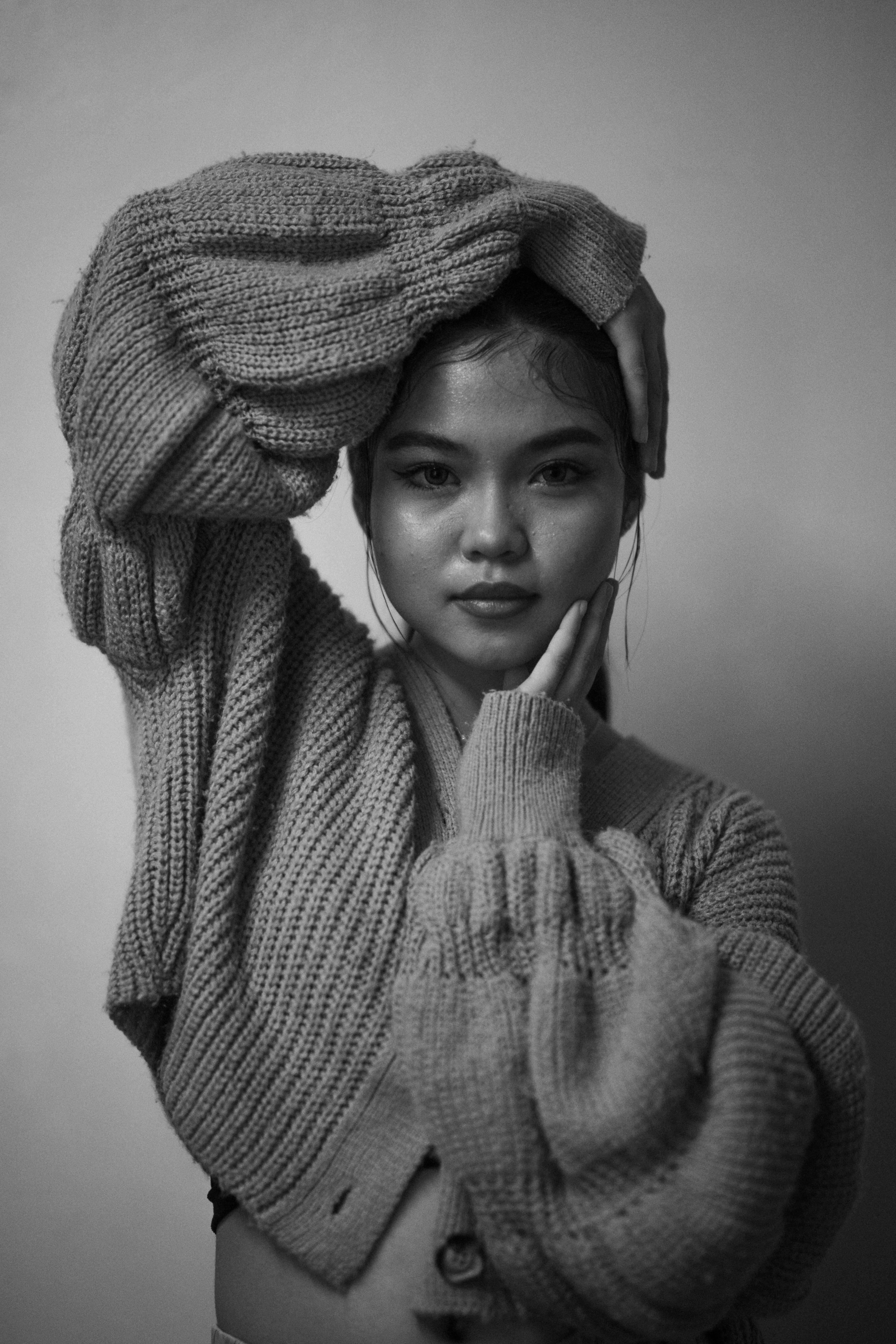 Stylish black and white portrait of an Asian woman in a cozy sweater posing indoors.