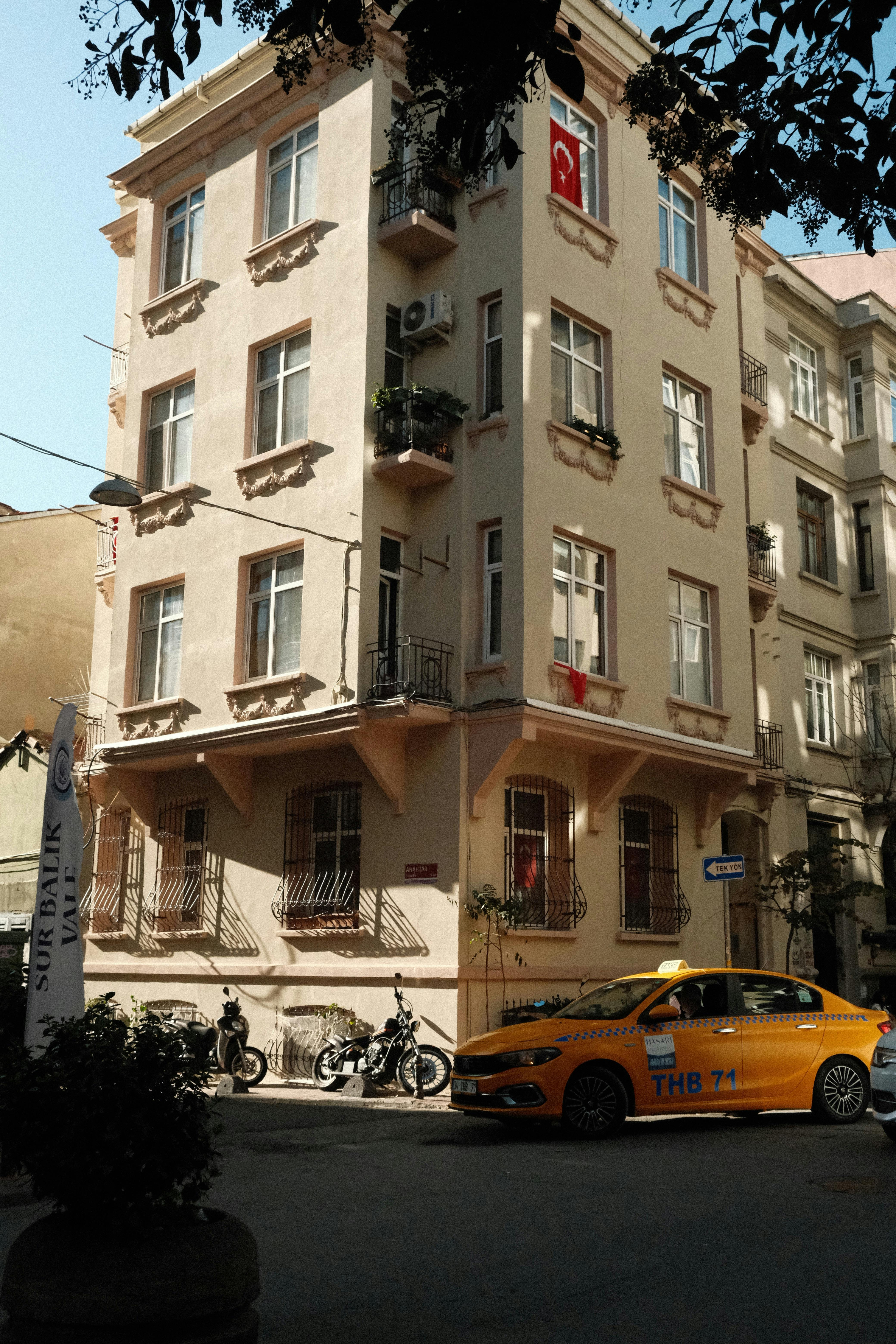 Free A sunny street in Istanbul featuring a townhouse facade and a yellow taxi in the foreground. Stock Photo