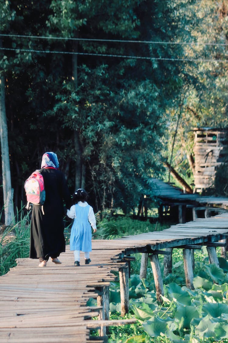 Back View Of A Mother And Little Daughter Walking On A Boardwalk 