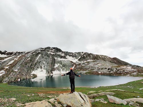 Man Standing on Rocks with Lake and Hill behind