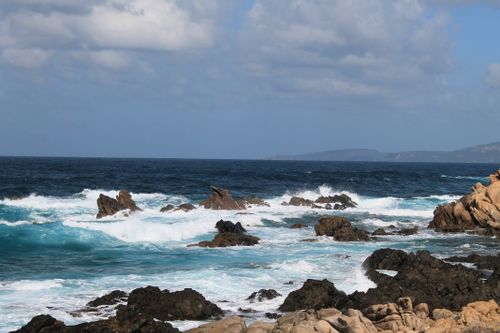 Free Dramatic view of ocean waves crashing on rocky shore under a bright blue sky. Stock Photo