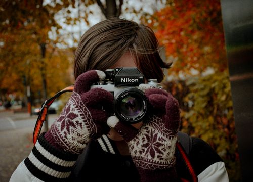 Free A person holding a vintage analog camera with gloves, capturing autumn colors outdoors. Stock Photo