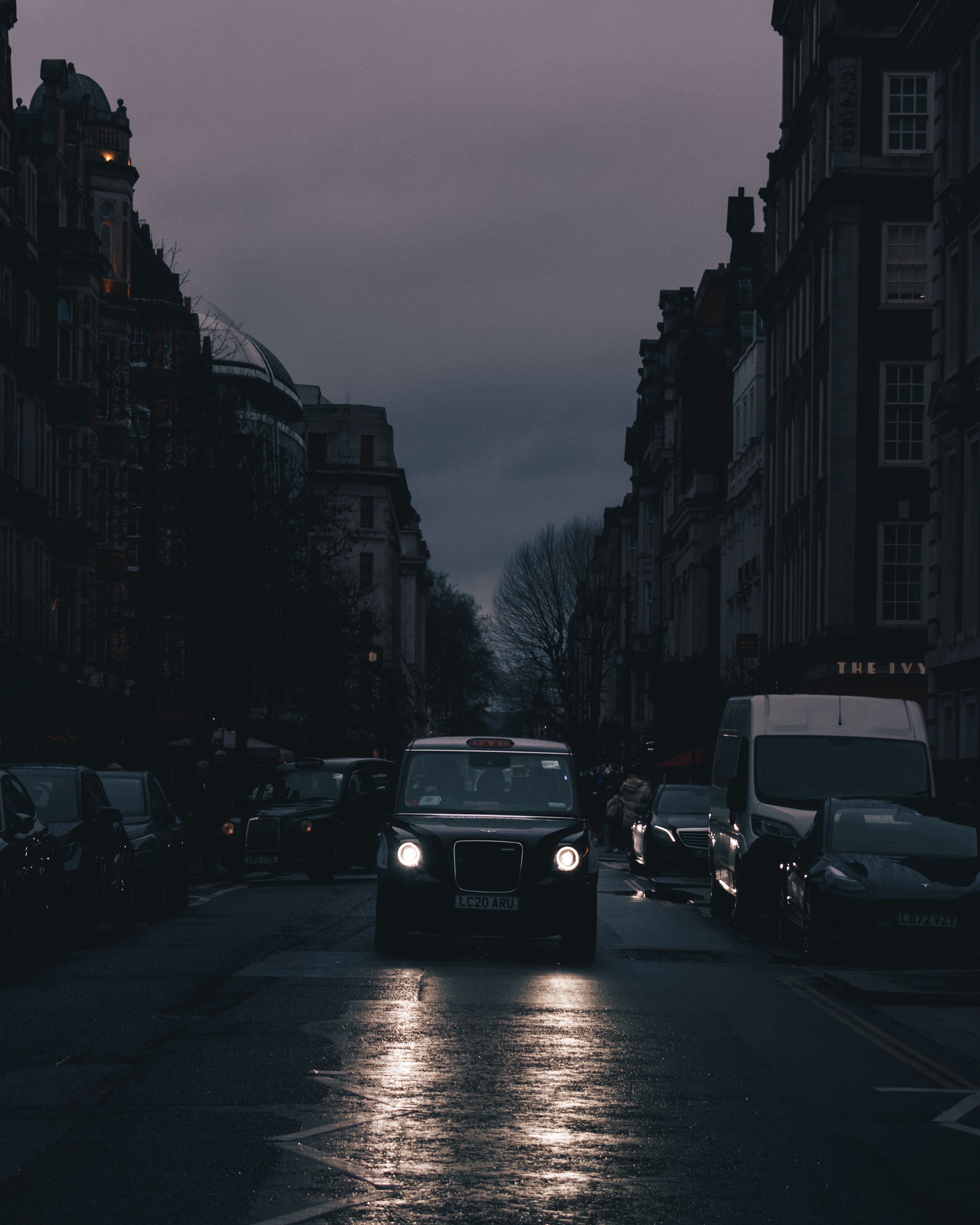 Capture a classic London taxi navigating dimly lit urban streets at dusk, showcasing city's moody ambiance.
