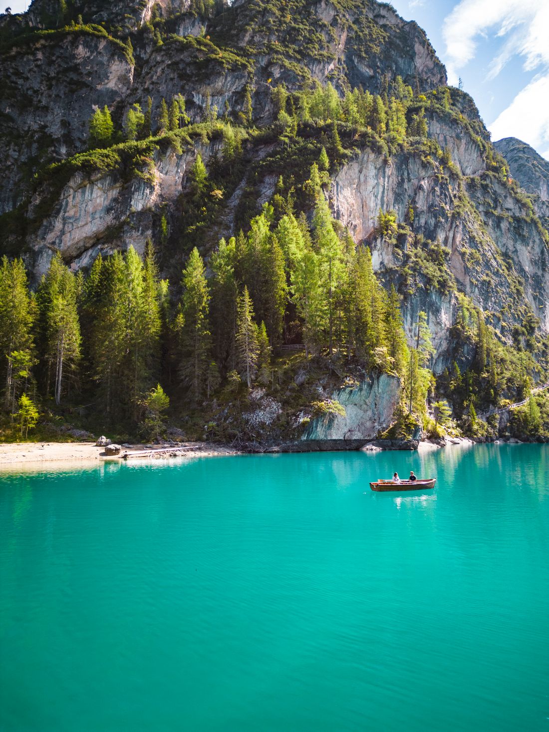 Travellers in a wooden rowing boat on the green water of Lago di Braies