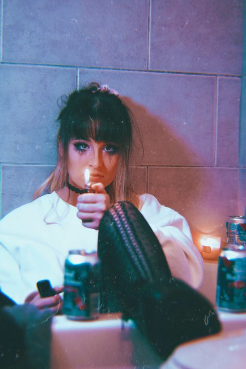 Free A woman holding a lighter, surrounded by Pabst cans and candles in a dimly lit room. Stock Photo
