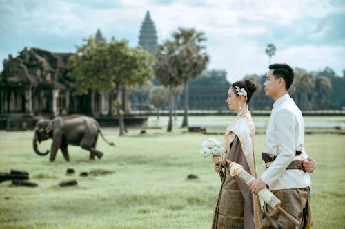 A couple in traditional attire standing in front of an elephant