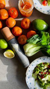 Vibrant flat lay of fresh citrus fruits, salad ingredients, and a stylish bottle.
