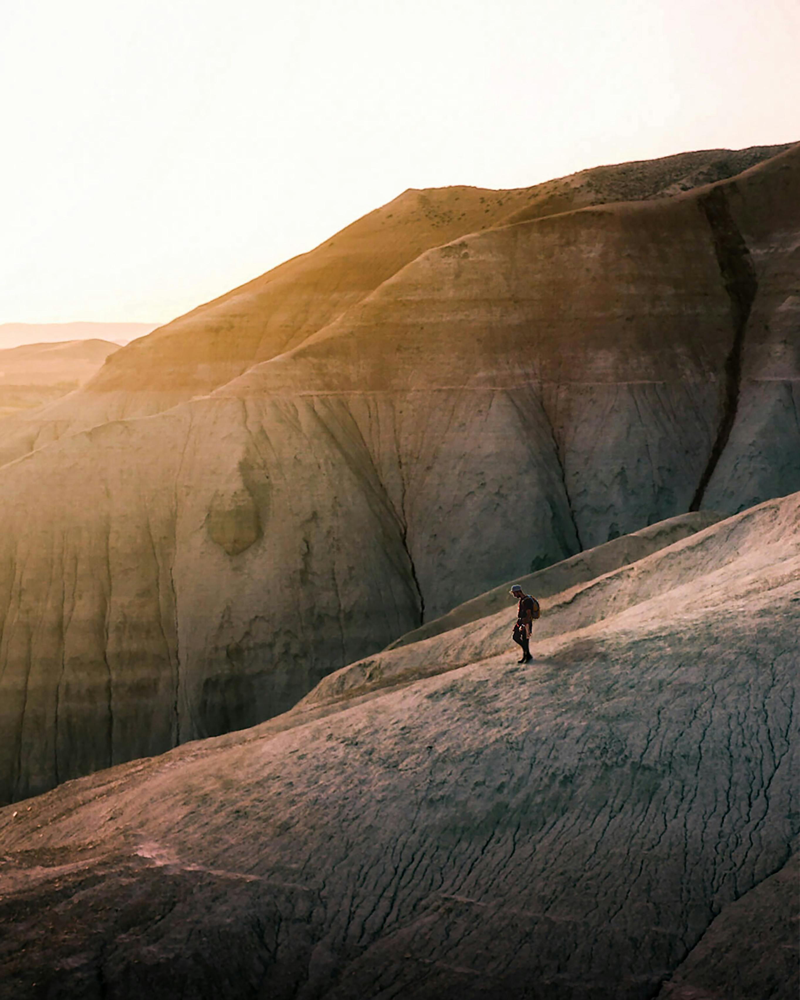 A lone hiker walks across rugged desert rocks, bathed in the warm hues of a sunset.
