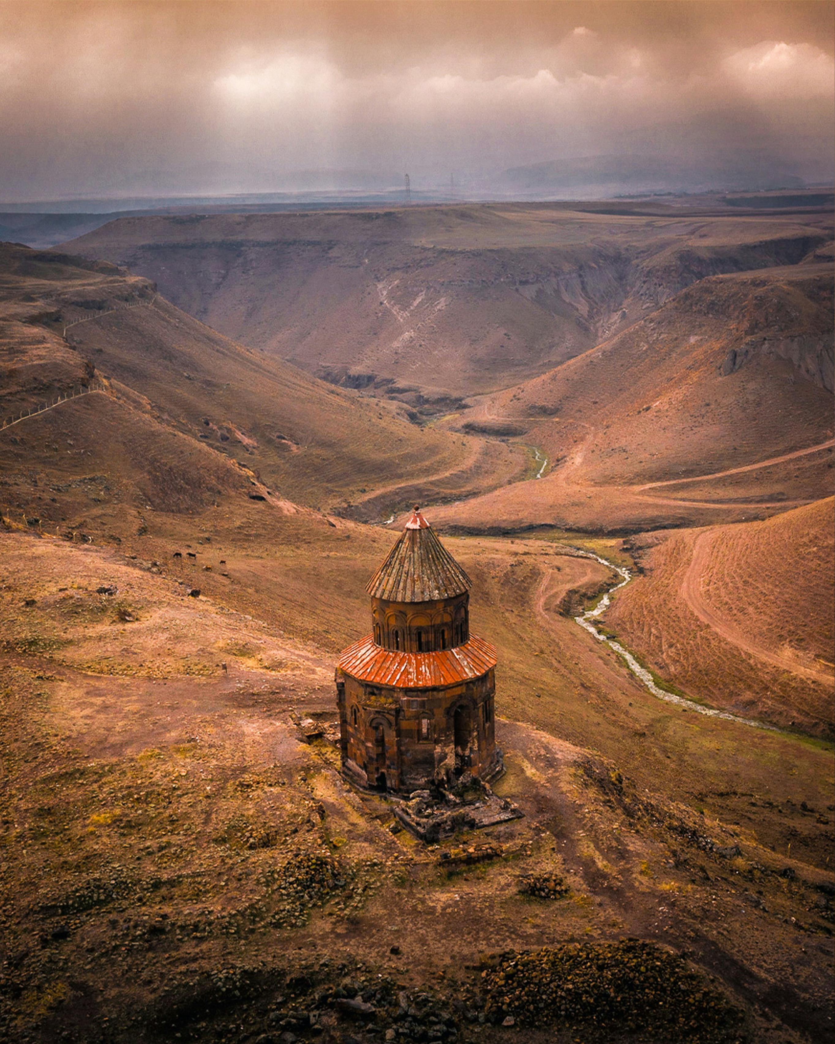 Captivating aerial shot of a historic chapel in a vast valley in Kars, Türkiye at sunset.