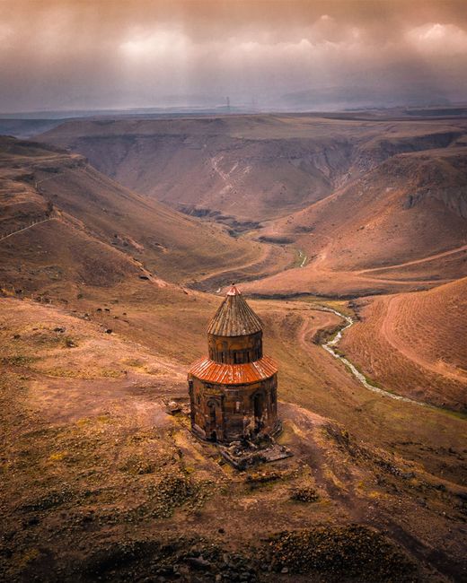 Captivating aerial shot of a historic chapel in a vast valley in Kars, Türkiye at sunset.