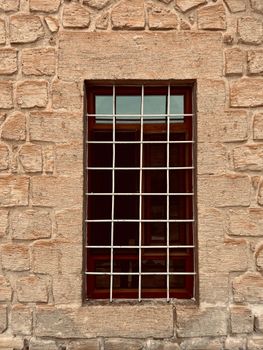 Close-up of a barred window set in a textured stone wall.