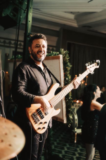 Smiling bass guitarist performing at an indoor event with lively atmosphere.