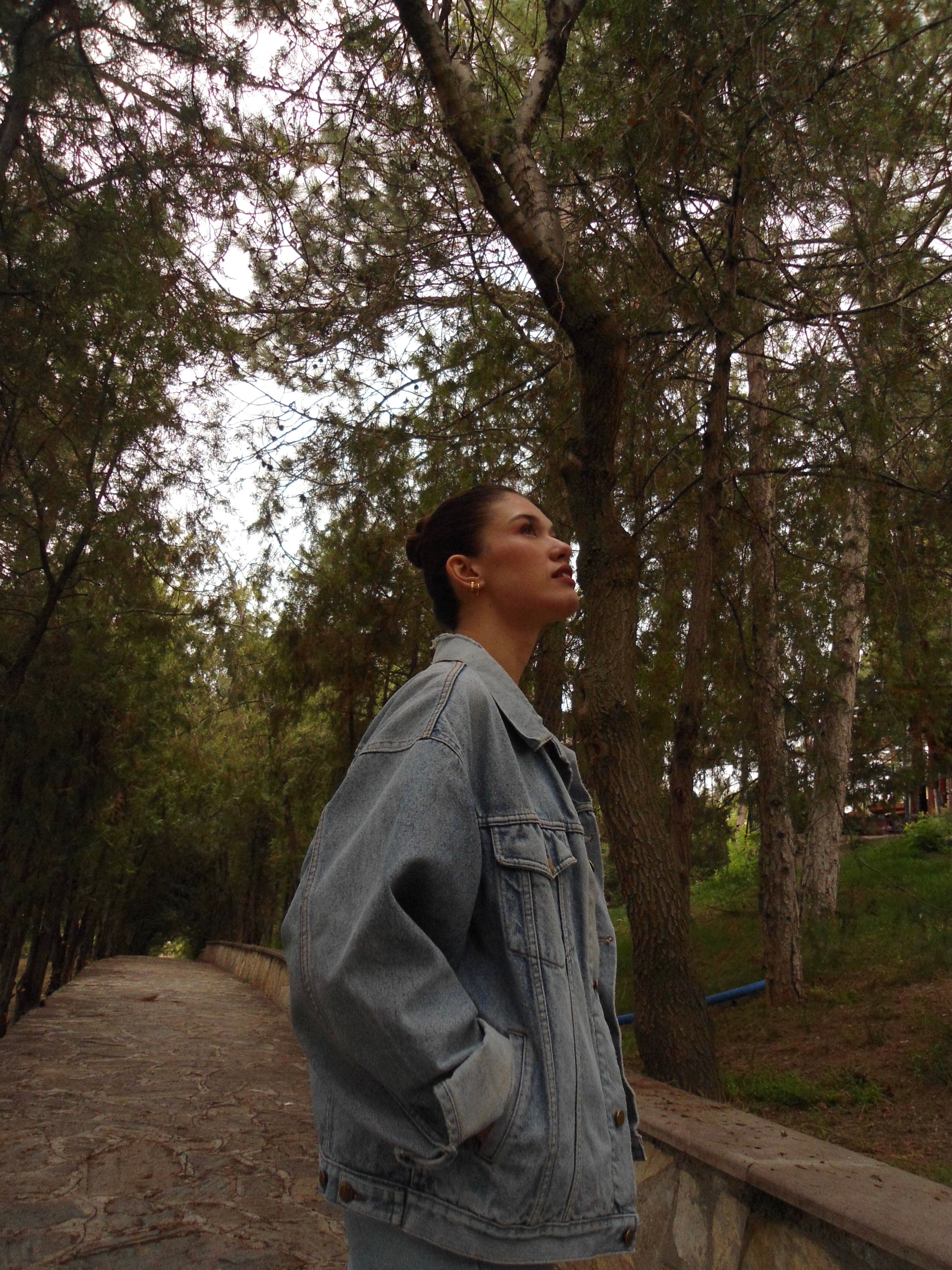 Portrait of a woman wearing a jean jacket standing among tall trees in a Konya park.