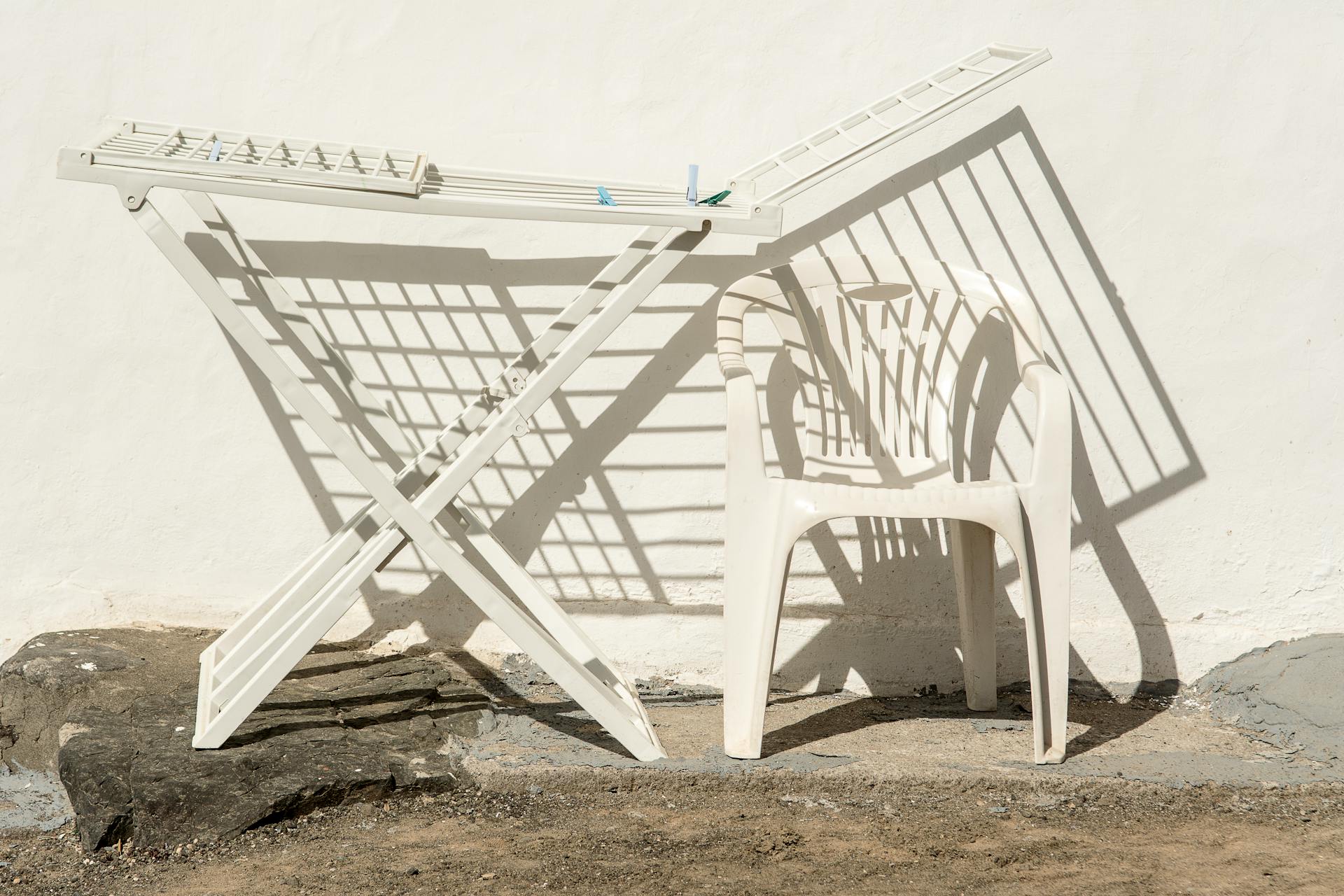 White plastic chair with drying rack casting shadows on a wall outdoors.