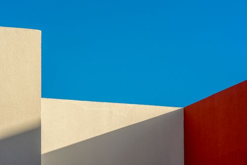 Free Minimalist photo of geometric building structures contrasting with a blue sky, showcasing shadows and colors. Stock Photo