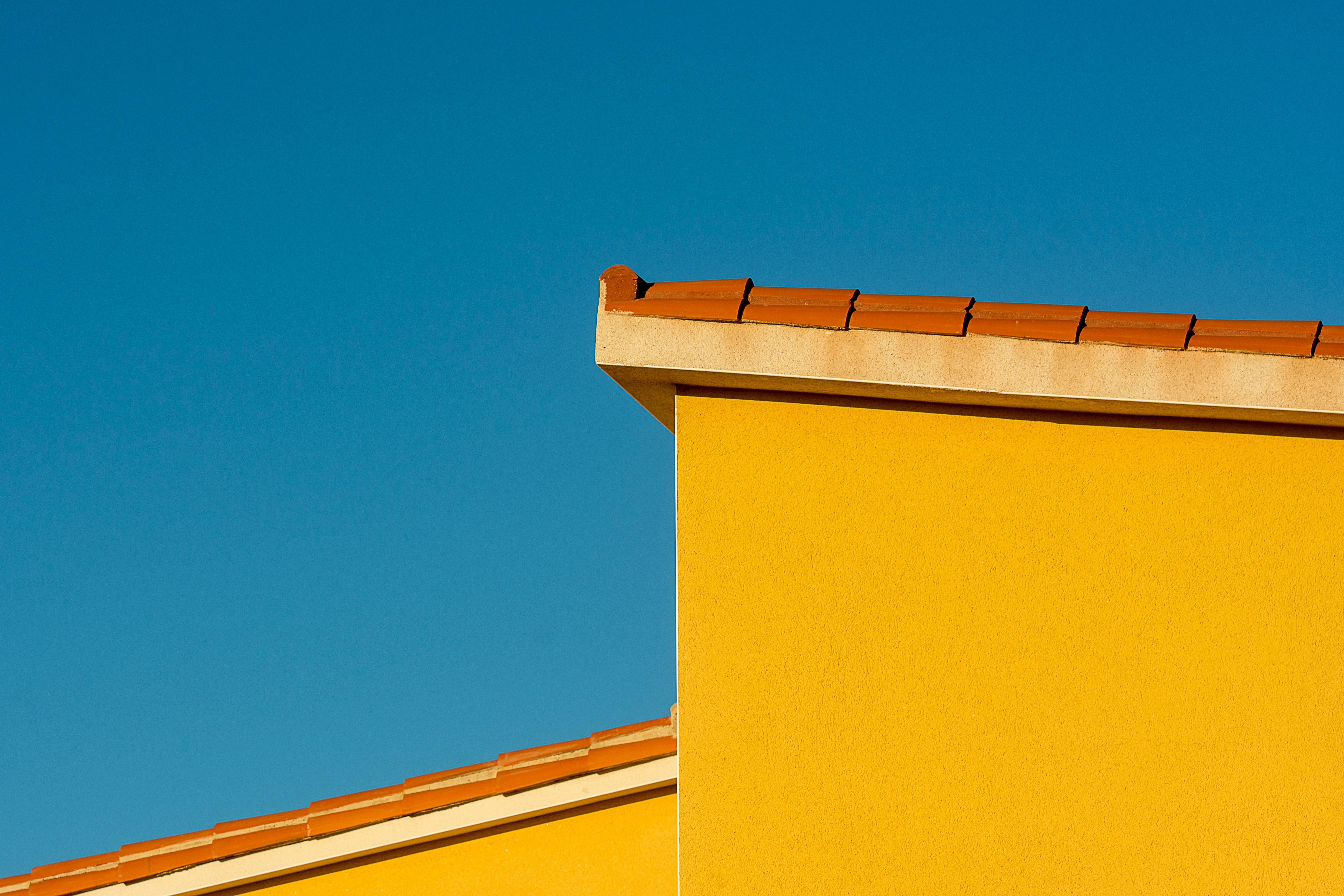 Minimalist yellow building facade with tile roof under clear blue sky.