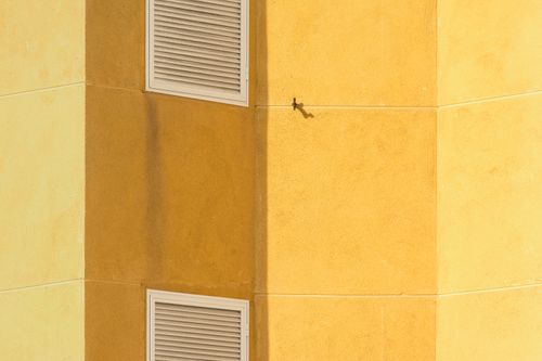 Free Close-up of a modern yellow building corner featuring ventilation grilles for architectural interest. Stock Photo