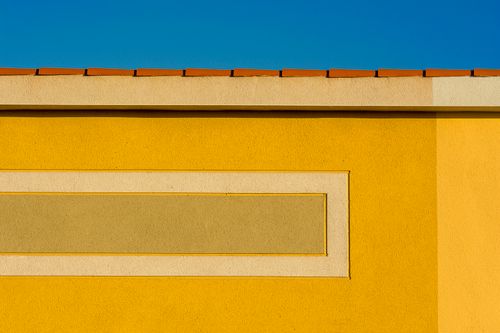 Free Bright yellow wall with terracotta rooftop against a clear blue sky, showcasing modern architectural design. Stock Photo