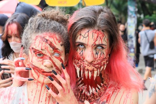 Gruesome zombie makeup on two women at a Halloween celebration outdoors.
