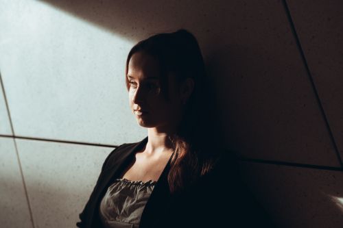 Free A woman stands against a wall in Berlin, highlighted by dramatic shadows and soft light. Stock Photo