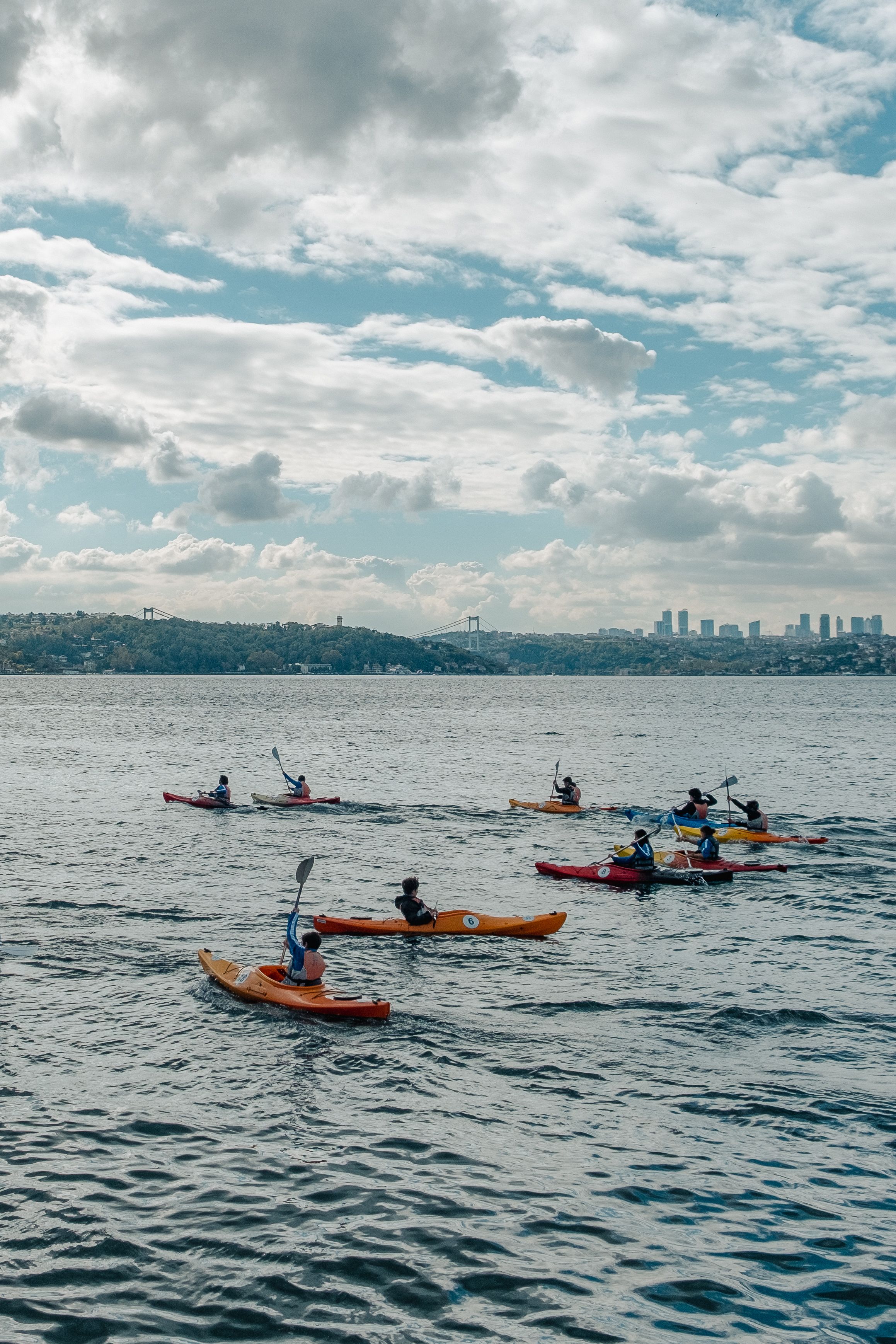 People kayaking on the Bosphorus Strait with a city skyline in the distance, capturing leisure and adventure.