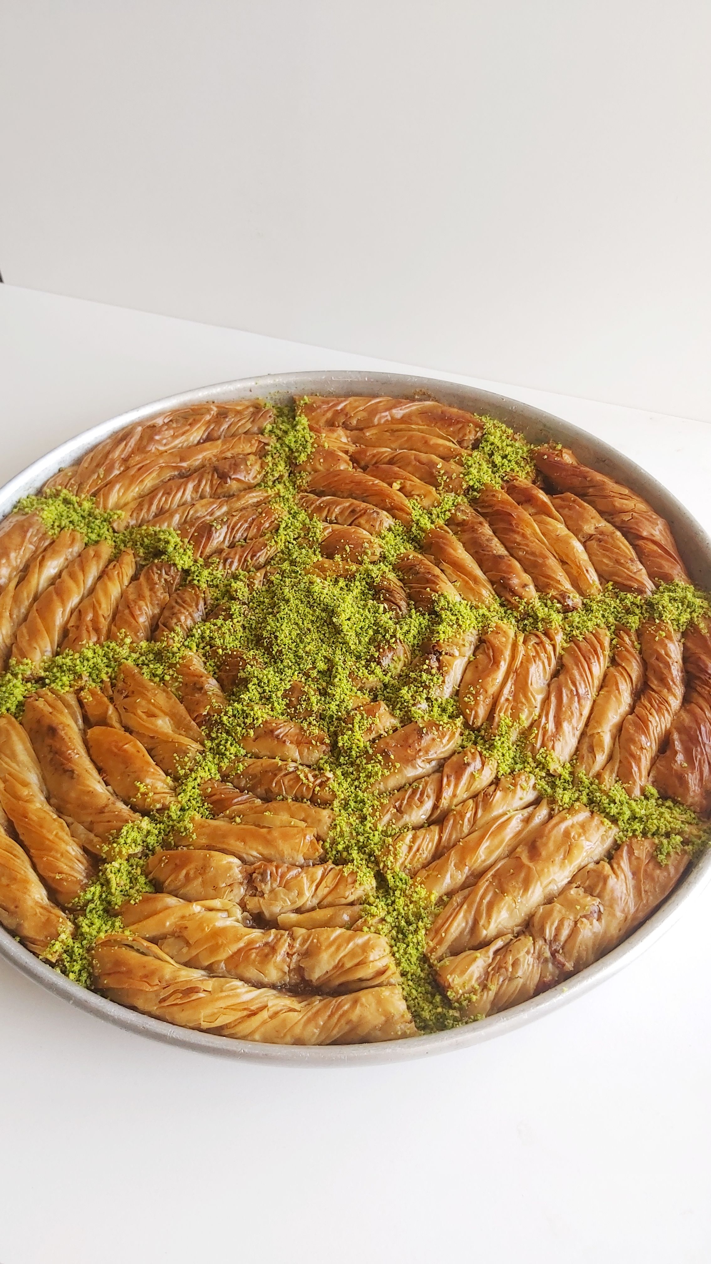 Close-up of a circular baklava tray with pistachio sprinkles on a white background.