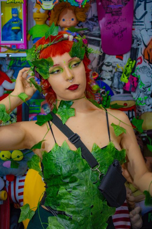 Free Vibrant portrait showcasing a woman in a unique leaf costume amidst colorful collectibles and posters. Stock Photo