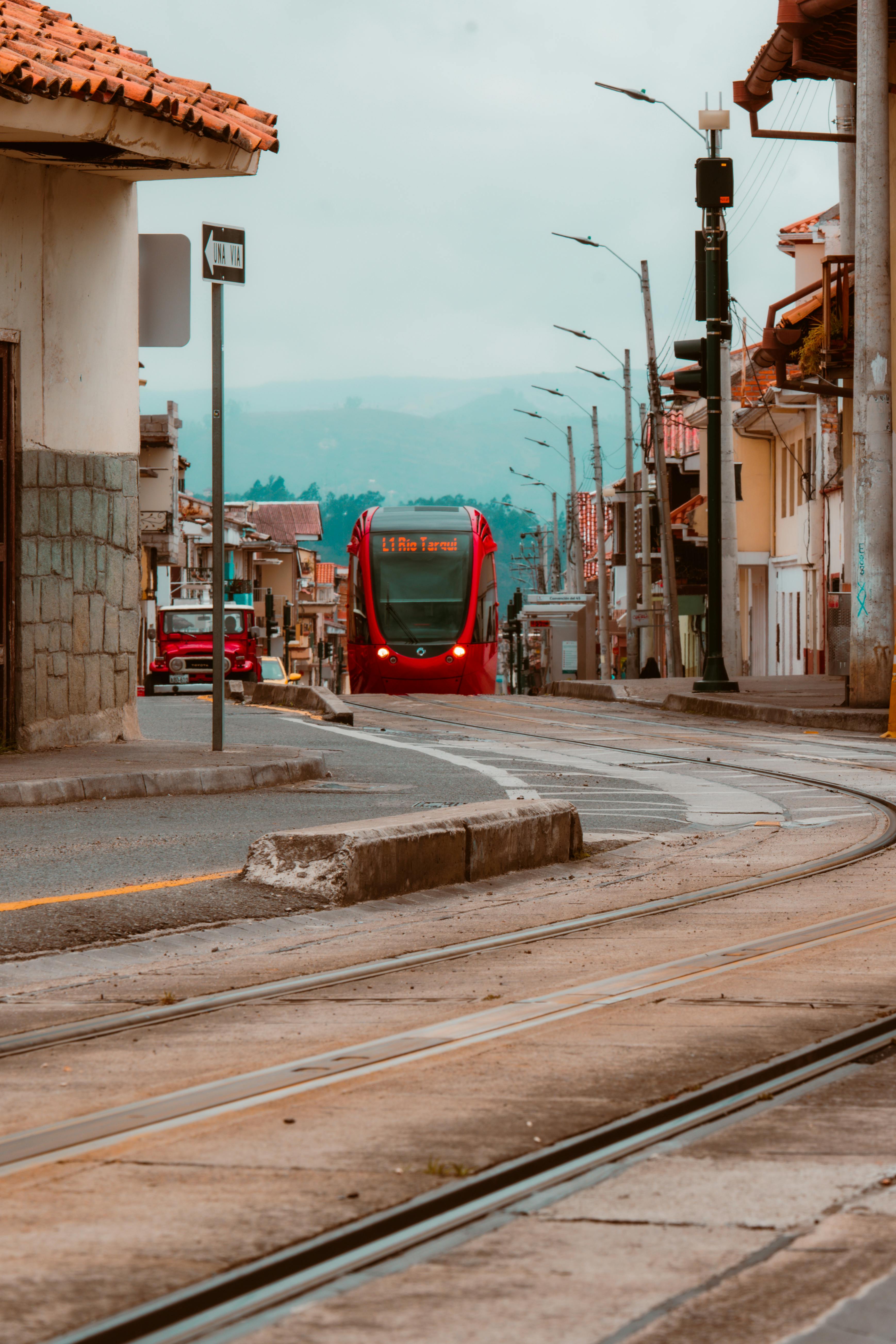 Free Red tram navigating through Cuenca's scenic streets, blending modern transportation with historic charm. Stock Photo