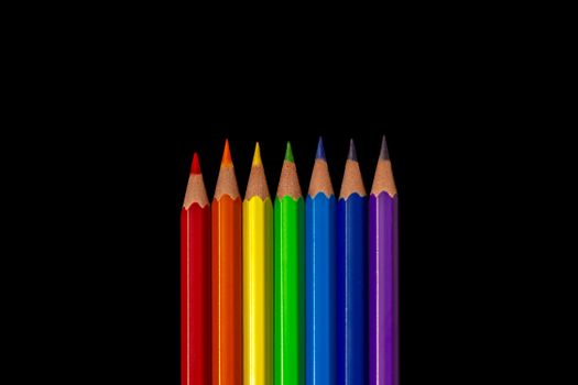 A close-up of seven colored pencils beautifully arranged against a black background.