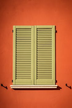 复古绿色百叶窗在充满活力的橙色墙壁上展现了建筑魅力