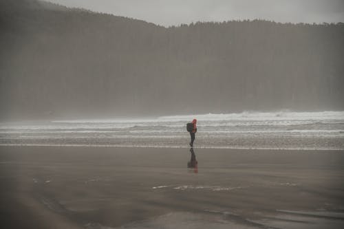 A Man with a Backpack Walking Alone on a Beach on a Foggy Day 