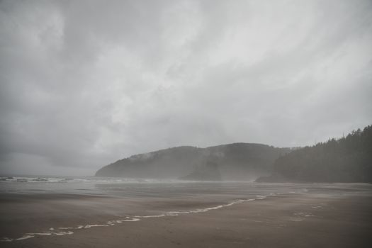 A serene beach with misty hills under an overcast sky, showcasing the tranquil ocean coastline.