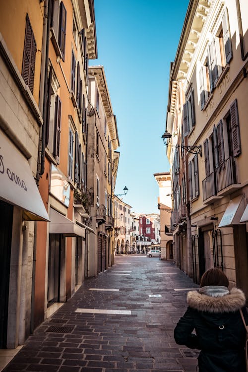 Woman in Parka Stands in Between Buildings