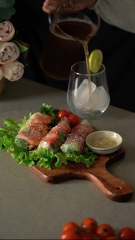 Tantalizing spring rolls on lettuce with sauce, paired with a refreshing iced drink being poured.