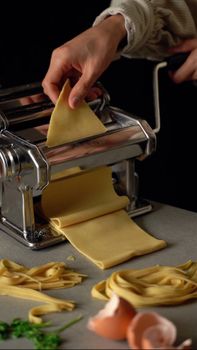 Close-up of hands making fresh pasta with a pasta machine at home.