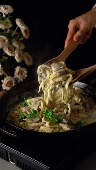 Delicious creamy pasta with herbs in a skillet, served with wooden spoons.