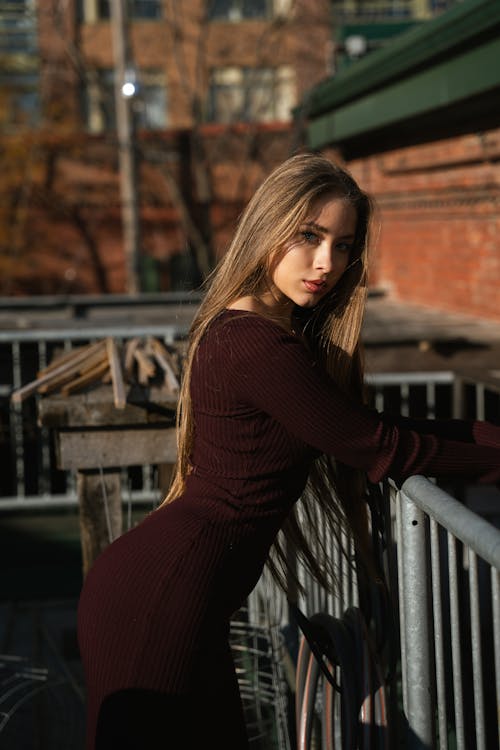 Young Woman in a Dress Standing by the Railing Outside 