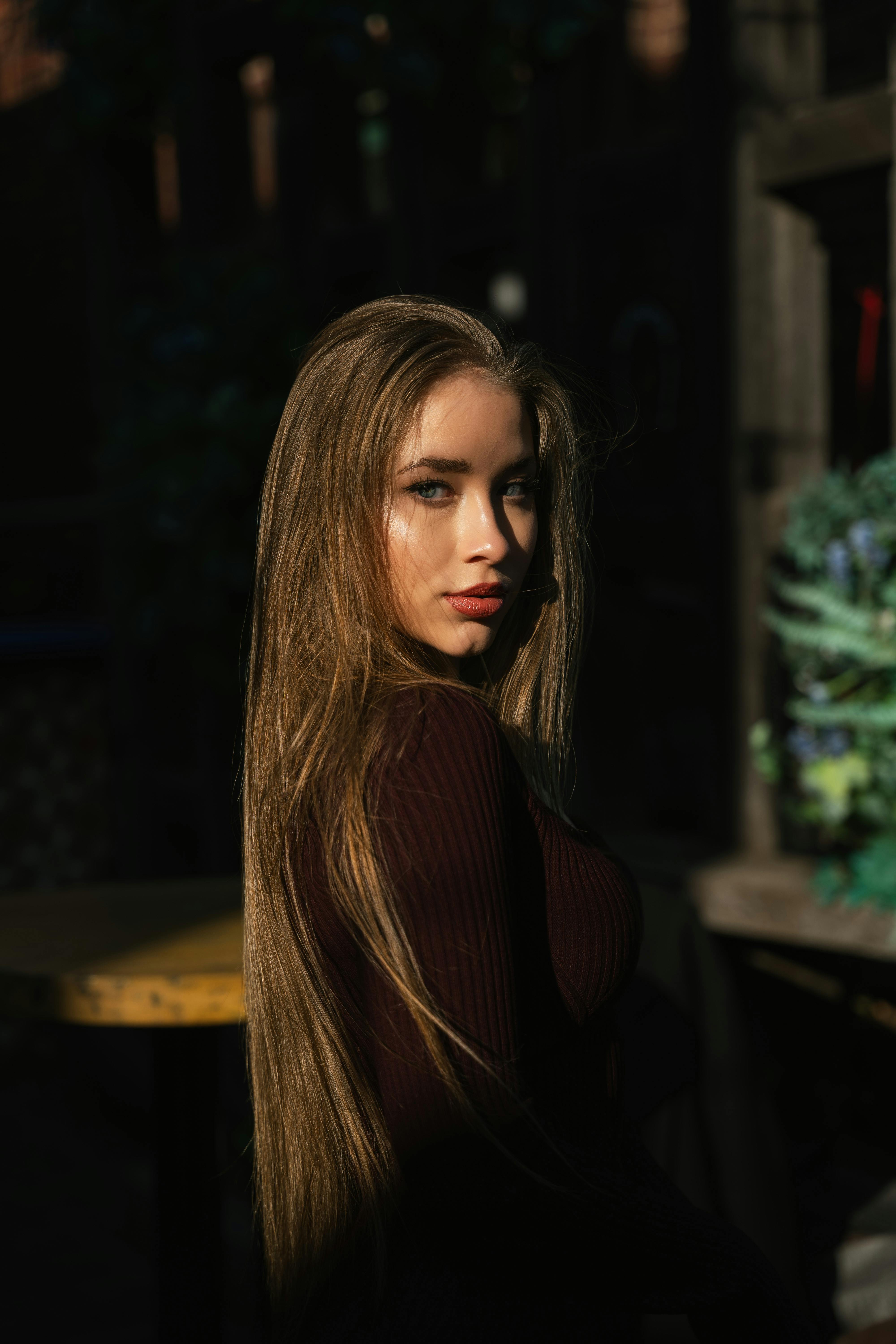 An elegant portrait of a young woman with long hair, captured in natural sunlight and a warm setting.