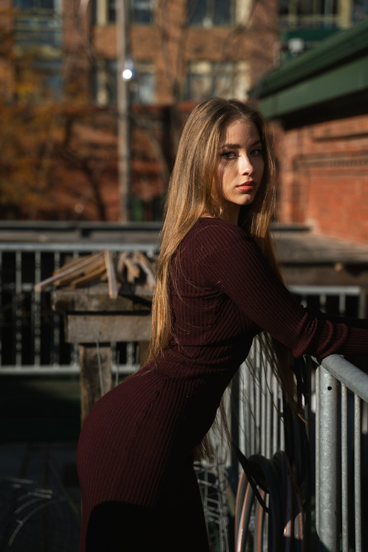 Young Woman In A Dress Standing By The Railing Outside 