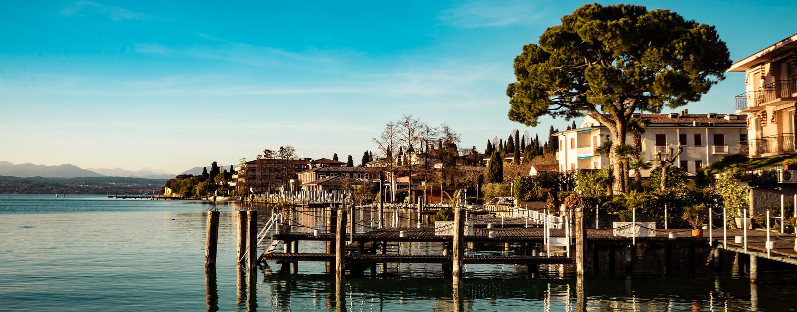Beautiful waterfront town by a lake with reflections of buildings, trees, and a pier under clear blue skies.