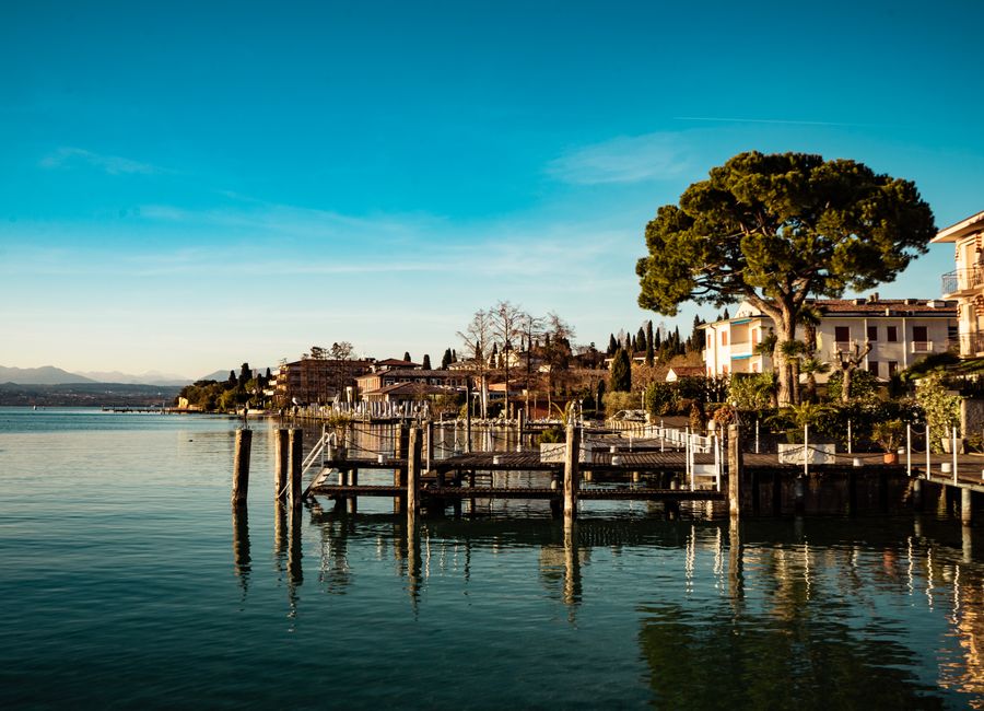 Beautiful waterfront town by a lake with reflections of buildings, trees, and a pier under clear blue skies.