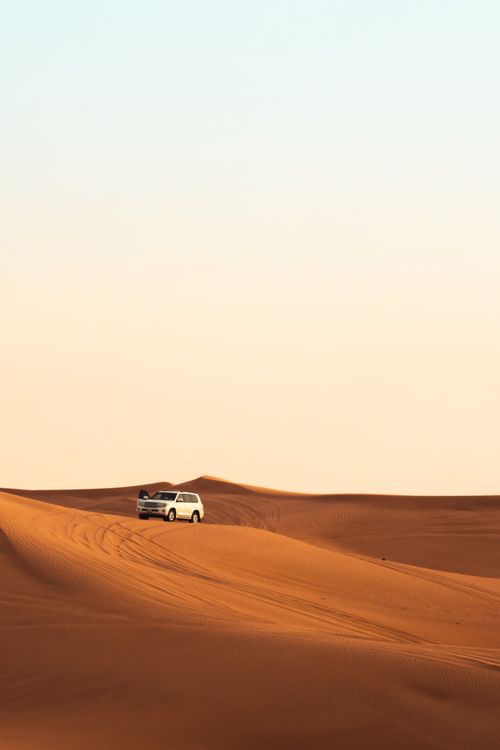 Free A white SUV navigating the golden sand dunes of the Dubai desert under a clear sky. Stock Photo