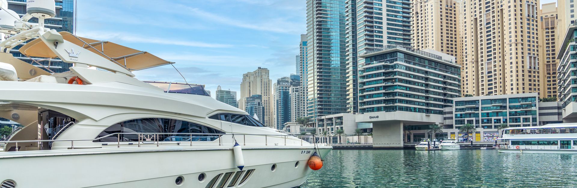 Elegant yacht docked at Dubai Marina against a backdrop of modern skyscrapers and clear blue sky.