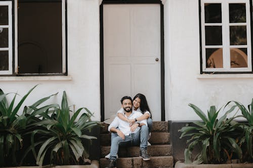 Smiling Woman Embracing Her Boyfriend Sitting on the Steps in Front of the House