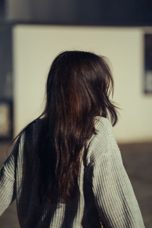 Free Brunette woman in a cozy sweater photographed from behind, creating a mysterious fashion vibe. Stock Photo