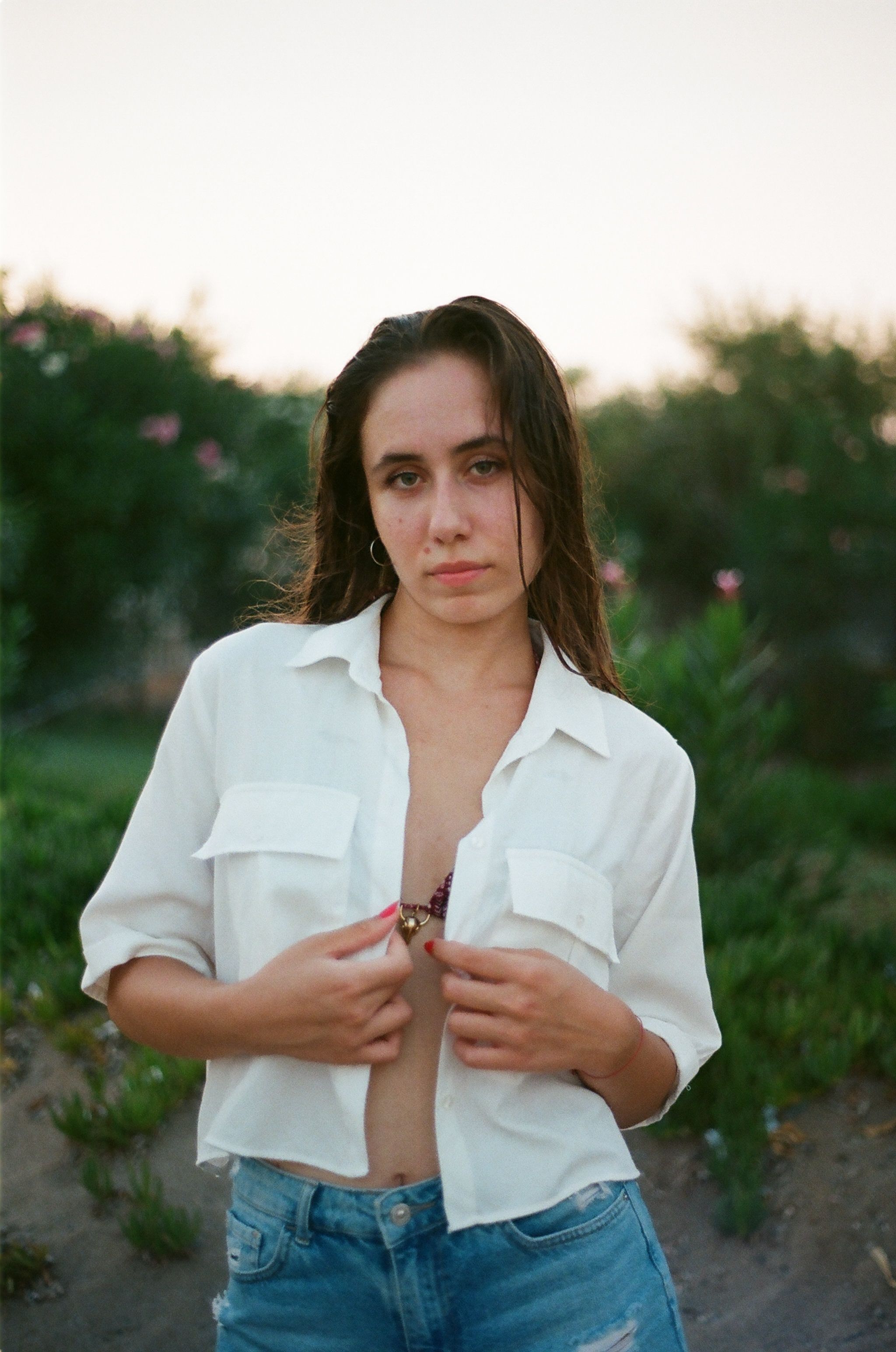 Outdoor portrait of a young woman in a white shirt and jeans, captured at sunset.