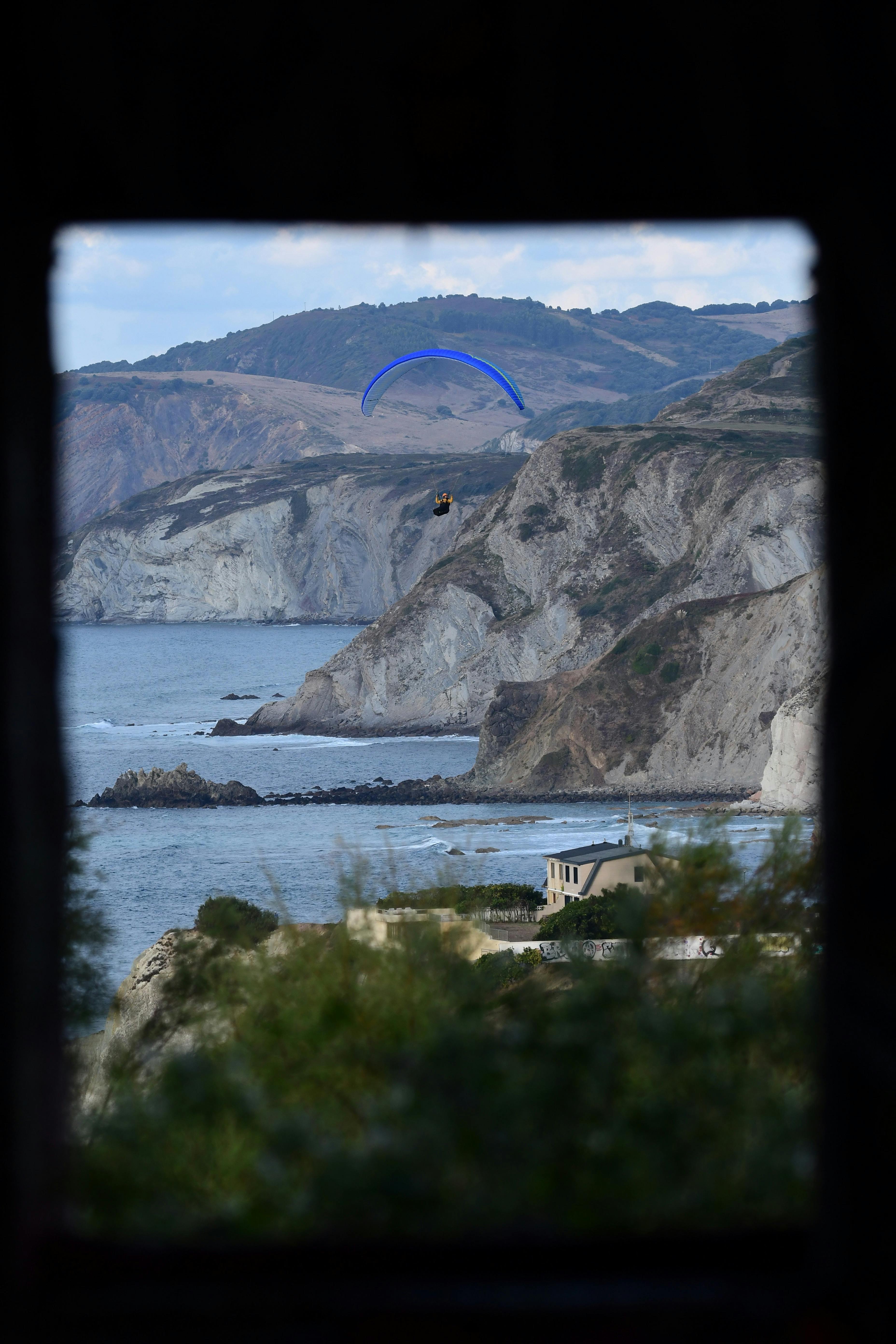 A lone paraglider gracefully flies over a stunning coastal cliff, offering a sense of freedom and adventure.