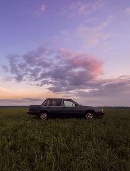 A vintage car sits in a grassy field under a serene sunset sky, conveying peace and nostalgia.